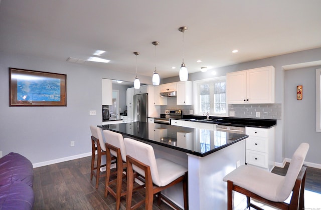 kitchen featuring dark countertops, appliances with stainless steel finishes, a breakfast bar, dark wood-style flooring, and backsplash