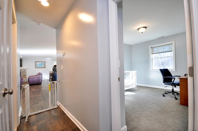 hall featuring baseboards, dark colored carpet, and dark wood-type flooring