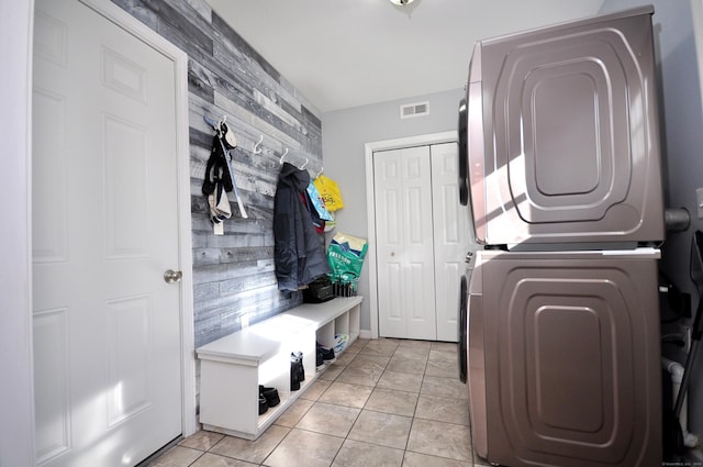 laundry area featuring stacked washer and clothes dryer, visible vents, an accent wall, light tile patterned flooring, and laundry area