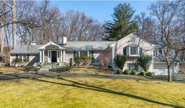 view of front facade with a chimney, aphalt driveway, and a front yard