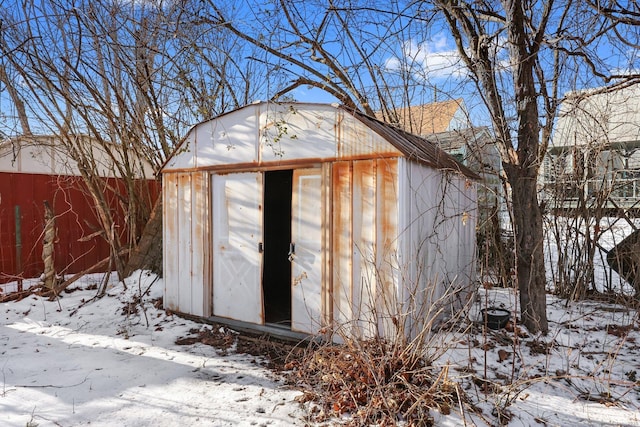 snow covered structure featuring an outbuilding, a storage unit, and fence