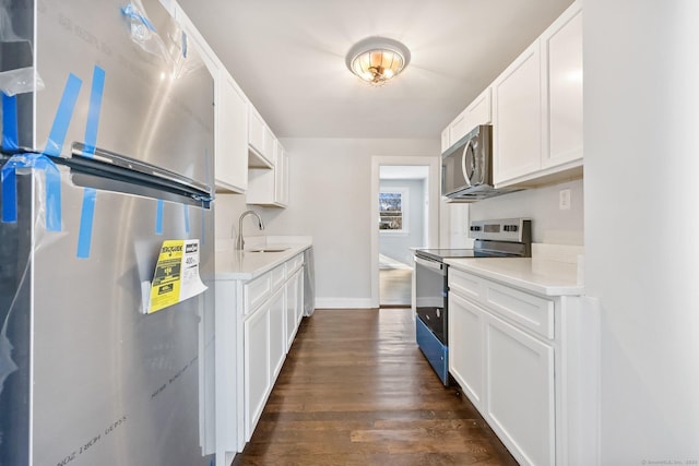 kitchen with light countertops, appliances with stainless steel finishes, dark wood-type flooring, white cabinets, and a sink