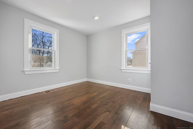 empty room featuring a healthy amount of sunlight, baseboards, visible vents, and dark wood finished floors