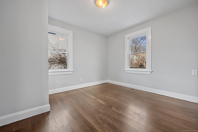 unfurnished room featuring dark wood-style floors, visible vents, and baseboards