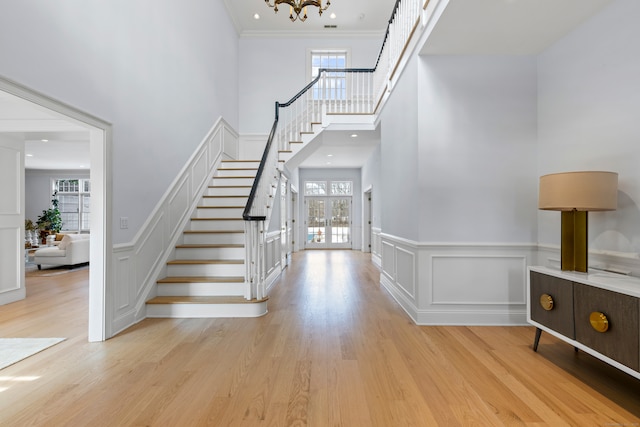 entryway with light wood-type flooring, a notable chandelier, stairs, and crown molding