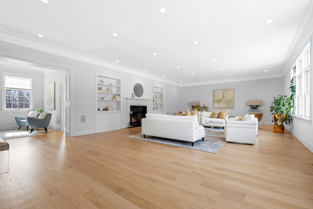 living area with a warm lit fireplace, baseboards, crown molding, light wood-type flooring, and built in shelves