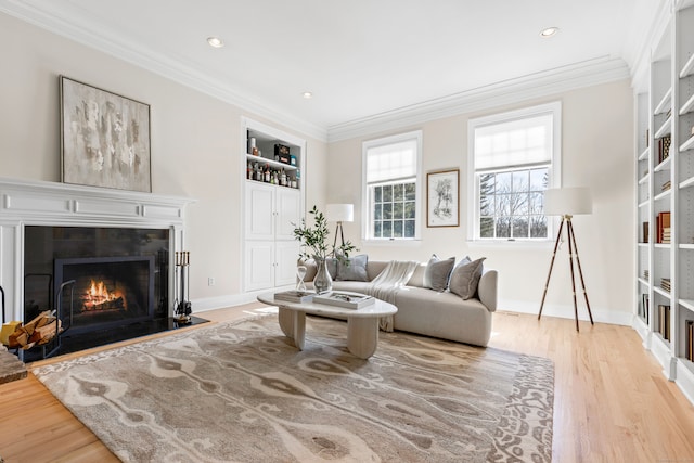 living area with a tile fireplace, built in shelves, crown molding, and wood finished floors