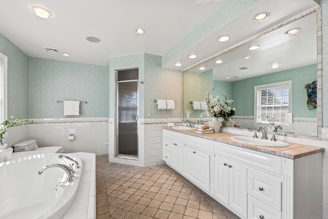 bathroom featuring a stall shower, a wainscoted wall, a sink, and wallpapered walls