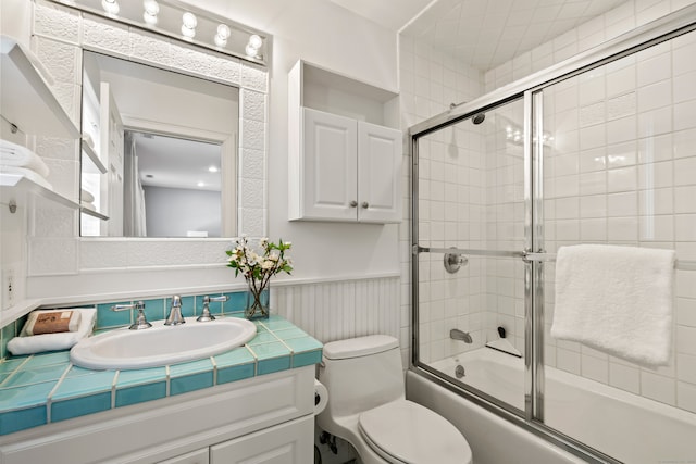 bathroom with a wainscoted wall, combined bath / shower with glass door, vanity, and toilet