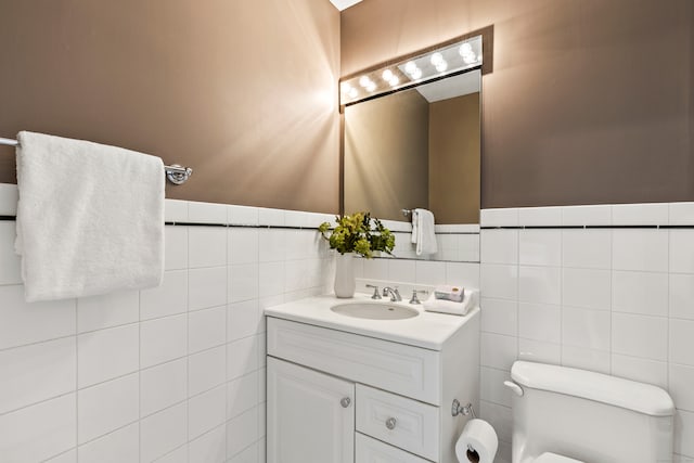 bathroom featuring toilet, wainscoting, vanity, and tile walls