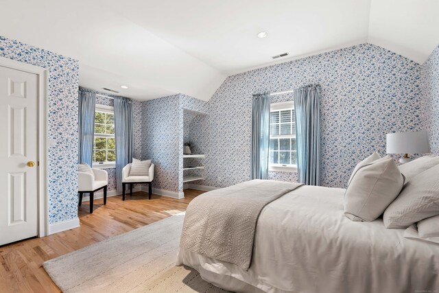 bedroom with wallpapered walls, visible vents, vaulted ceiling, and wood finished floors