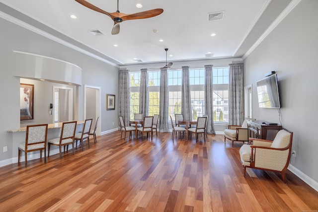 living area with a ceiling fan, visible vents, crown molding, and wood finished floors