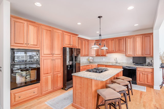 kitchen featuring a kitchen island, a sink, light wood-style floors, backsplash, and black appliances