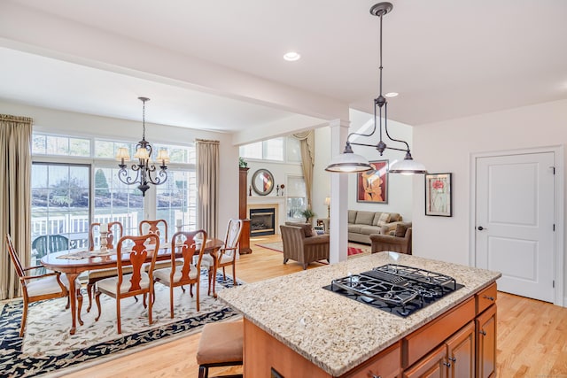 kitchen with black gas cooktop, light wood-style flooring, open floor plan, light stone countertops, and a glass covered fireplace