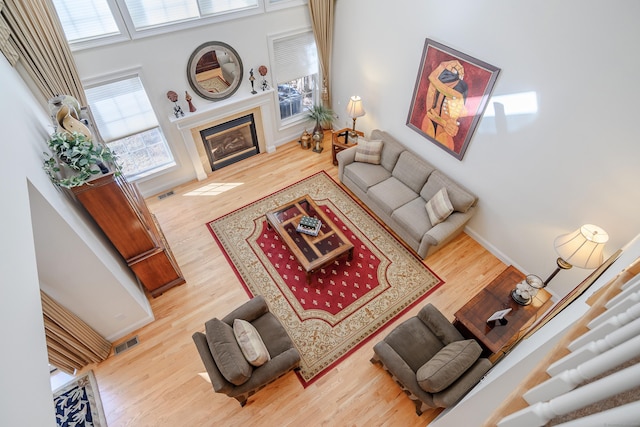 living room featuring baseboards, a fireplace with flush hearth, visible vents, and wood finished floors