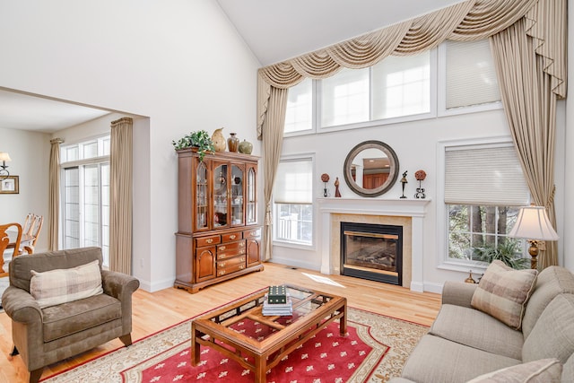 living area with high vaulted ceiling, a fireplace, baseboards, and wood finished floors