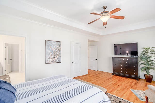 bedroom with a tray ceiling, crown molding, light wood-style flooring, a ceiling fan, and baseboards