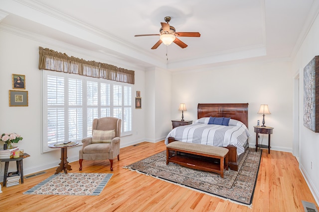 bedroom with a raised ceiling, visible vents, and wood finished floors