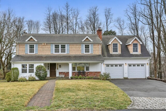 view of front of property featuring a front lawn, aphalt driveway, covered porch, a garage, and a chimney