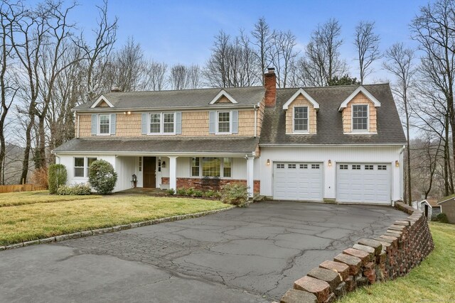 view of front facade featuring driveway, a front lawn, covered porch, an attached garage, and a chimney