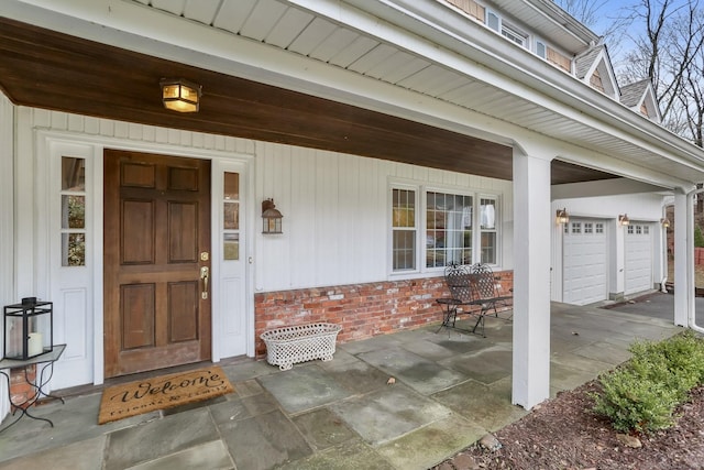 view of exterior entry with a porch, a garage, and brick siding