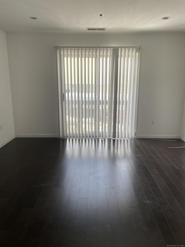 unfurnished room featuring dark wood-type flooring, visible vents, and baseboards