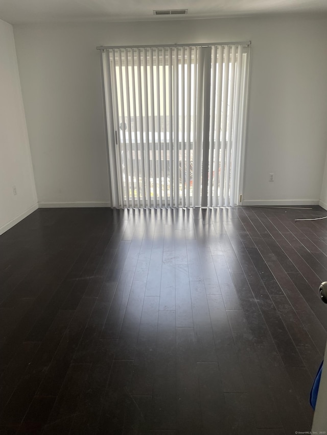 unfurnished room with dark wood-type flooring, visible vents, and baseboards