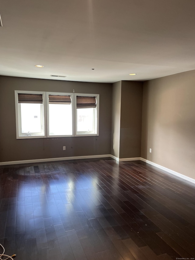 empty room with dark wood-style floors, recessed lighting, visible vents, and baseboards