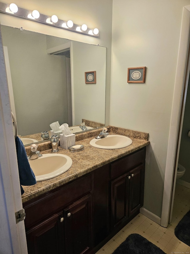 bathroom with a sink, toilet, and double vanity