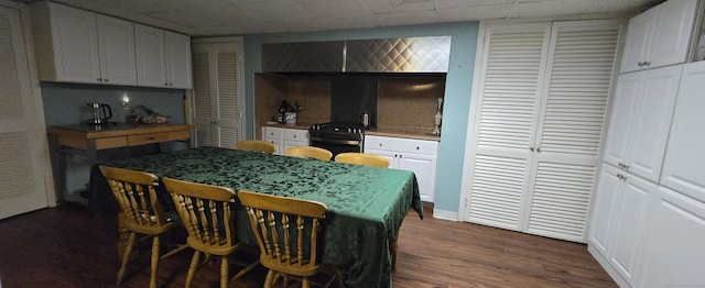 kitchen with a kitchen breakfast bar, tasteful backsplash, dark wood finished floors, black / electric stove, and white cabinets