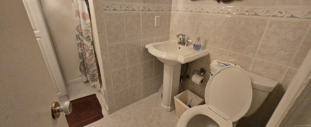 bathroom featuring toilet, a sink, a shower with shower curtain, tile walls, and tile patterned flooring