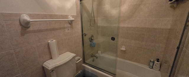 bathroom featuring bath / shower combo with glass door, tile walls, and toilet