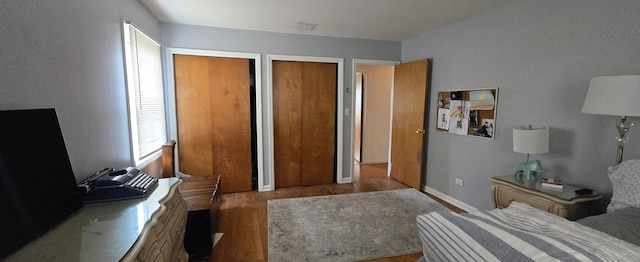 bedroom with baseboards, two closets, and wood finished floors
