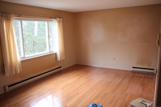 unfurnished room featuring a baseboard heating unit, light wood-type flooring, and baseboards