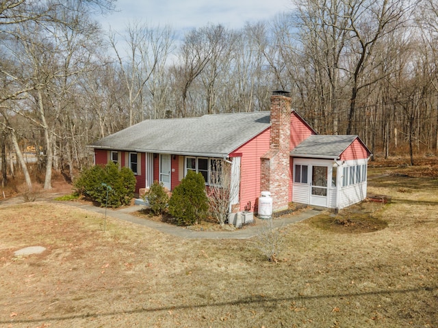 view of front of property with a sunroom, a chimney, a front lawn, and roof with shingles