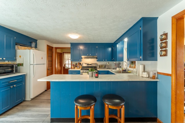 kitchen with appliances with stainless steel finishes, blue cabinets, a peninsula, under cabinet range hood, and a sink