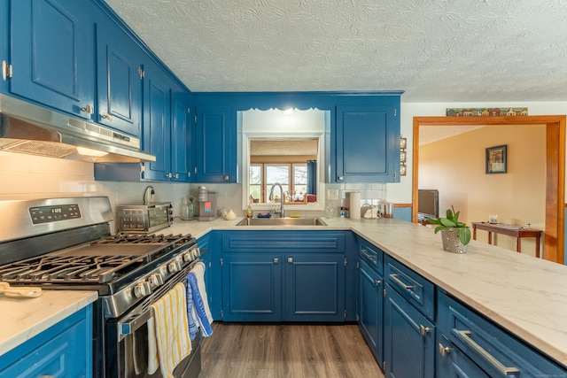 kitchen with blue cabinets, stainless steel gas stove, a sink, and under cabinet range hood