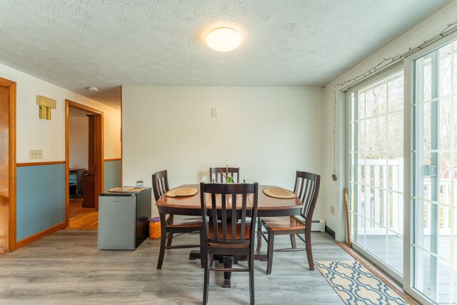 dining space featuring a textured ceiling, baseboards, and wood finished floors