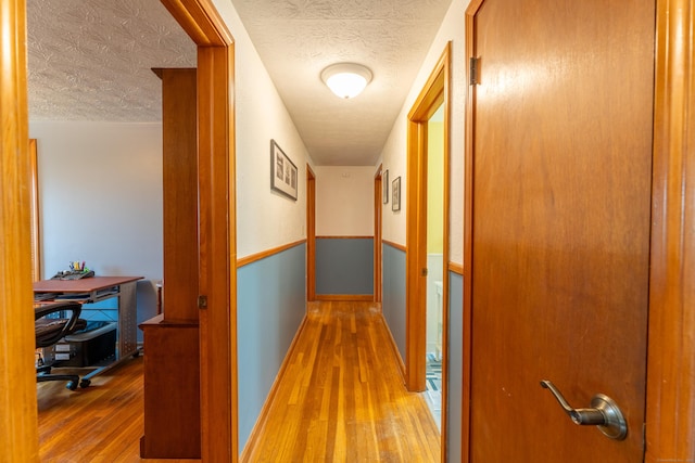 hall with a textured ceiling and wood finished floors