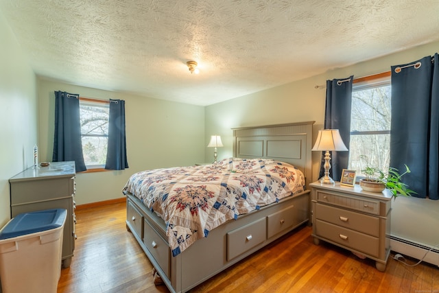 bedroom featuring a baseboard heating unit, multiple windows, and wood finished floors