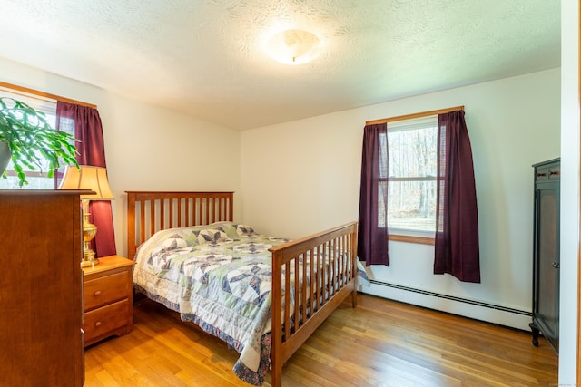 bedroom featuring a baseboard heating unit, a textured ceiling, and wood finished floors