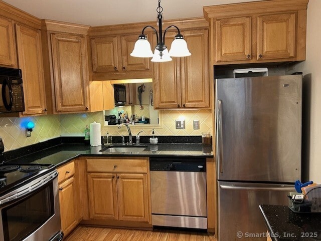 kitchen with brown cabinets, backsplash, appliances with stainless steel finishes, a sink, and light wood-type flooring