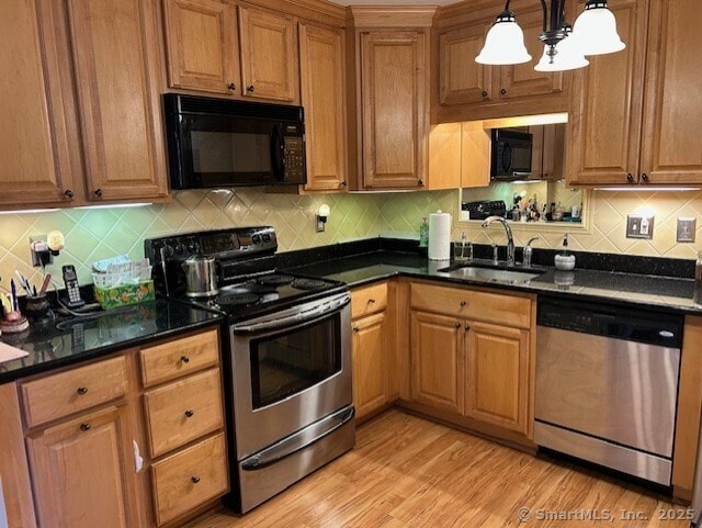 kitchen with decorative light fixtures, light wood finished floors, stainless steel appliances, decorative backsplash, and a sink