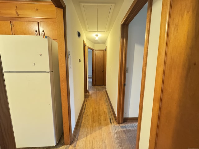 corridor with attic access, light wood-type flooring, and baseboards