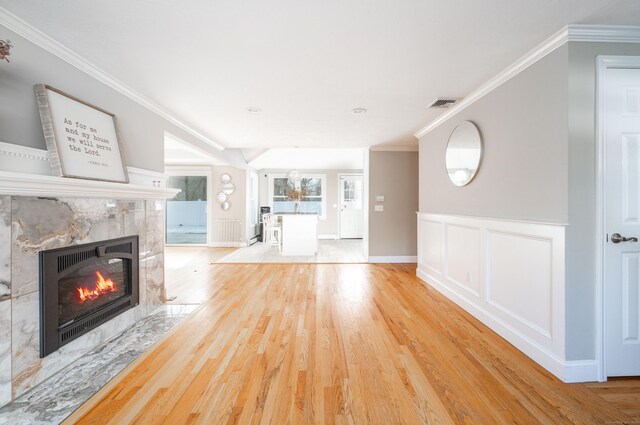 unfurnished living room featuring a decorative wall, a fireplace, visible vents, ornamental molding, and light wood-type flooring