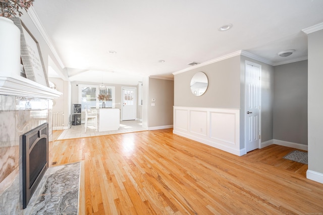 unfurnished living room featuring a premium fireplace, visible vents, baseboards, ornamental molding, and light wood-type flooring