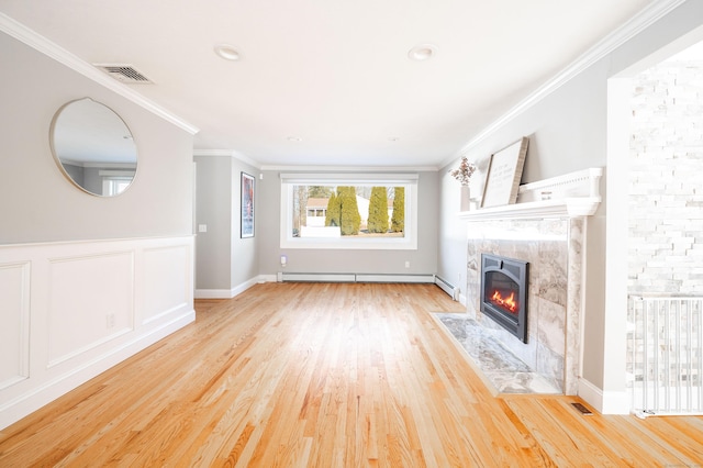 unfurnished living room featuring a baseboard heating unit, a premium fireplace, wood finished floors, visible vents, and crown molding