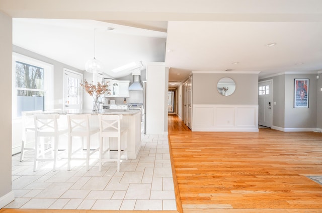 kitchen with white cabinets, ornamental molding, a kitchen breakfast bar, decorative light fixtures, and light countertops