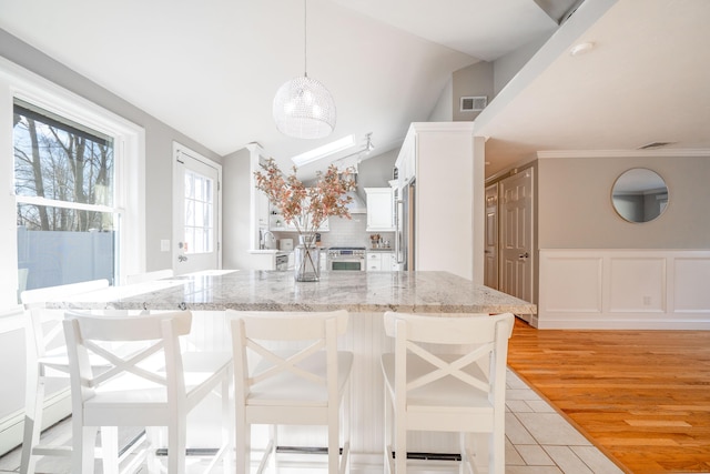 kitchen featuring stainless steel appliances, visible vents, a kitchen bar, and white cabinetry