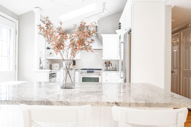 kitchen featuring tasteful backsplash, light stone countertops, high quality appliances, and white cabinets